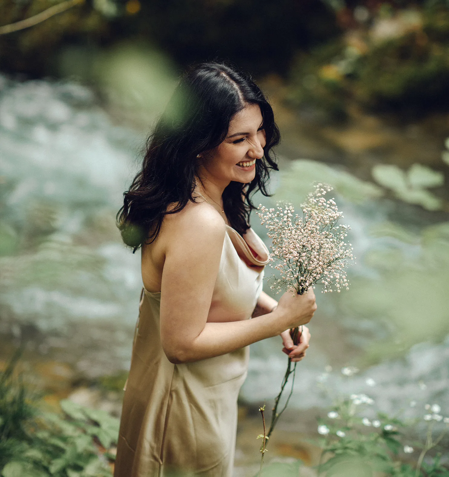 Yasemin souriante tenant un bouquet de fleurs au bord d'une rivière